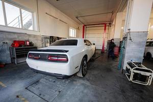 mecânico na estação de reparação de serviço trabalhando com muscle car. homem trabalhador levanta o carro para diagnosticar o chassi. foto