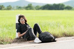mulher sente-se com mochila pedindo carona ao longo de uma estrada foto