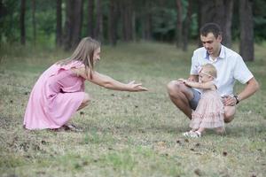 marido, esposa e seus pequeno filha para uma andar dentro a parque. feliz Papai e mãe Ensinar uma um ano de idade bebê para andar. foto