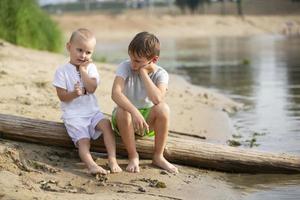 dois irmãos, a mais velho e a mais jovem, estão jogando de a rio. crianças em a arenoso costa conversa e saciar. foto