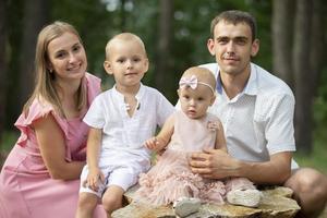 marido e esposa e seus pequeno crianças. família retrato dentro natureza. mãe e Papai estão posando com seus irmão e irmã. jovem família com crianças para uma andar dentro a madeiras. foto