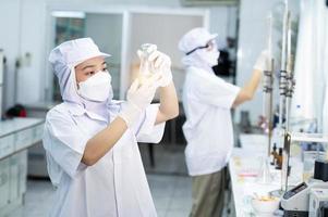 ásia fêmea especialista dentro qualidade ao controle laboratório examinando tomate ingrediente Comida dentro pesquisa laboratório, Comida indústria foto