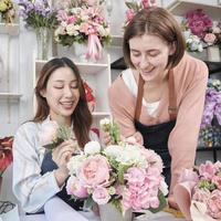 duas jovens e belas parceiras floristas organizando e decorando um ramo de flores juntas sorriem com um trabalho feliz em uma floricultura colorida com flores frescas, pequeno empresário de pequenas empresas. foto