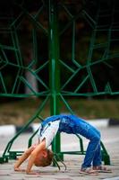 uma pequeno menina faz uma ponte, dobrar dela costas dentro rua . uma flexível criança, fazendo ginástica exercícios. foto