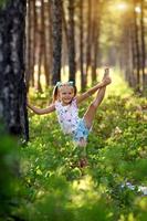 a pequeno menina levanta dela perna acima, ginástica exercícios dentro a floresta. foto