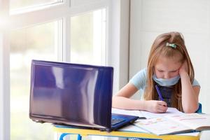 a menina faz conectados lições, trabalho de casa. Internet escola, distância aprendizado, quarentena. foto