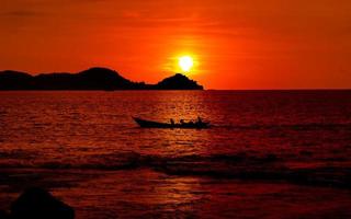 lindo oceano pôr do sol panorama com ilha e pescador barco dentro silhueta foto