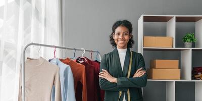 retrato sorrir Preto mulher trabalhando em roupas dentro alfaiataria ateliê. atraente lindo jovem fêmea moda desenhador sorrir depois de sucesso dentro faço Novo feito à mão terno dentro oficina. foto