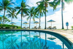 belo guarda-sol de luxo e cadeira ao redor da piscina ao ar livre em hotel e resort com coqueiro no céu do pôr do sol foto