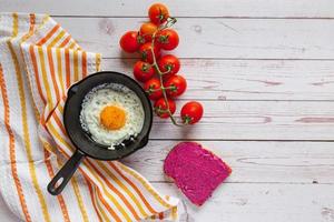 café da manhã tempo, frito ovo dentro uma fundida ferro panela com salada tigela , beterraba espalhar e fresco cereja tomates em de madeira mesa foto