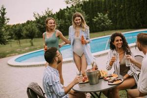 grupo de jovens torcendo com cidra à beira da piscina no jardim foto