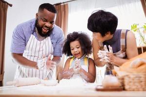 feliz africano americano família apreciar juntos enquanto preparar a farinha para fazer biscoitos às casa foto