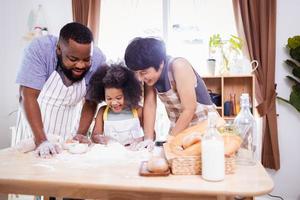 feliz africano americano família apreciar juntos enquanto preparar a farinha para fazer biscoitos às casa foto