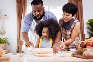 feliz africano americano família apreciar juntos enquanto preparar a farinha para fazer biscoitos às casa foto