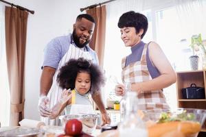 feliz africano americano família apreciar juntos enquanto preparar a farinha para fazer biscoitos às casa foto