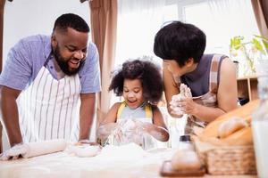 feliz africano americano família apreciar juntos enquanto preparar a farinha para fazer biscoitos às casa foto