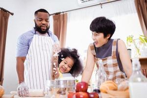 feliz africano americano família apreciar juntos enquanto preparar a farinha para fazer biscoitos às casa foto