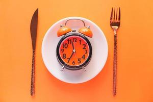 despertador no prato em fundo laranja foto