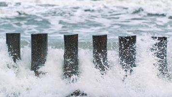 altos quebra-mares de madeira em ondas do mar espumantes foto