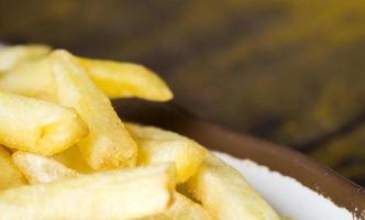 batatas fritas em um prato branco com borda marrom na mesa de madeira foto