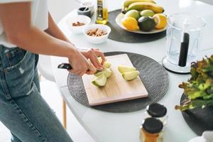 jovem fino mulher dentro branco camiseta e azul jeans cozinhando batido com maçãs saudável Comida dentro cozinha às casa foto