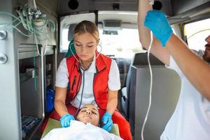 médicos com ferido paciente dando a infusão . jovem masculino paramédicos segurando iv solução. fêmea médico listagem coração do paciente foto