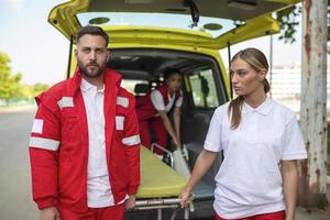 jovem paramédicos comovente ambulância maca a partir de carro. paramédicos dentro uniforme levando maca Fora a ambulância carro foto