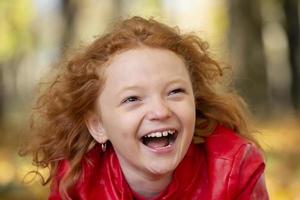alegre ruivo menina rindo alegremente contra a pano de fundo do a outono parque. foto