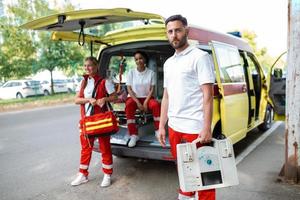 paramédico enfermeira e emergência médico às ambulância com kit. uma paramédico, em pé às a traseiro do a ambulância, de a aberto portas foto