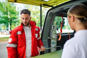 dois paramédicos com uma maca perto a ambulância. paramédicos dentro uniforme levando maca Fora a ambulância carro foto