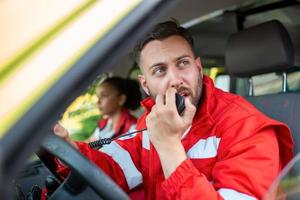 bonito jovem masculino paramédico falando de portátil rádio enquanto sentado dentro ambulância foto
