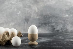 ovo de galinha cru em uma xícara de ovo com uma caixa de ovo em um fundo de mármore foto