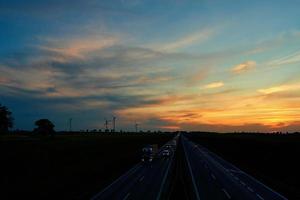 rodovia com carro tráfego e moinho de vento turbinas às pôr do sol foto