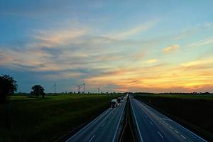 rodovia com carro tráfego e moinho de vento turbinas às pôr do sol foto