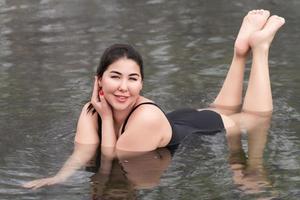 jovem mulher dentro Preto uma pedaço tomando banho roupa de banho deitado dentro ao ar livre piscina às spa, quente molas resorts foto