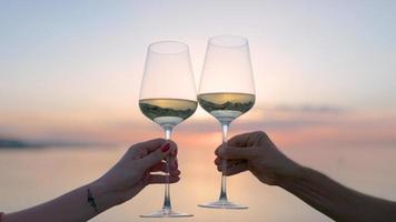 dois mãos fazer uma Felicidades com vinho vidro contra espumante mar e céu às pôr do sol foto
