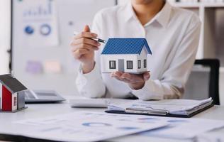 modelo de casa com agente imobiliário e cliente discutindo contrato para comprar casa, seguro ou empréstimo de fundo imobiliário.