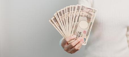 mão de uma mulher segurando a pilha de notas de iene japonês. dinheiro de mil ienes. dinheiro do japão, impostos, economia de recessão, inflação, investimento, finanças e conceitos de pagamento de compras foto