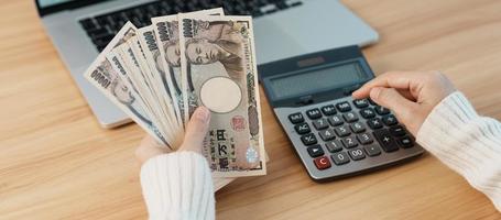 mão de mulher contando notas de iene japonês com calculadora. dinheiro de mil ienes. dinheiro do japão, imposto, economia de recessão, inflação, investimento, finanças, salários e conceitos de pagamento foto