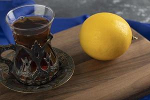 um copo de chá com limão em uma tábua de madeira foto