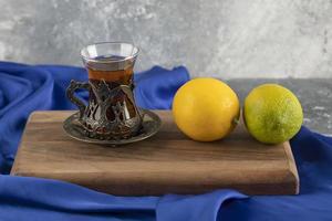 um copo de chá com limões em uma tábua de madeira