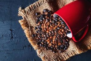 grãos de café derramando de uma caneca vermelha foto