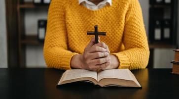 mãos juntas em oração a deus junto com a bíblia no conceito cristão e religião, mulher reza na bíblia na mesa de madeira foto