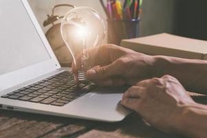uma pessoa segurando uma lâmpada ao lado de um laptop, conceito de novas ideias foto