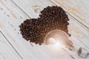 grãos de café em forma de coração e uma lâmpada em uma mesa de madeira foto