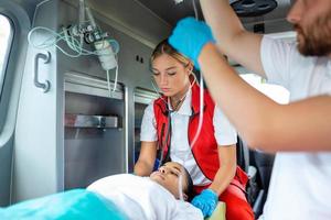 médicos com ferido paciente dando a infusão . jovem masculino paramédicos segurando iv solução. fêmea médico listagem coração do paciente foto