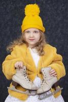 lindo pequeno menina dentro inverno roupas com branco patins. cinco anos criança dentro uma tricotado amarelo chapéu. foto