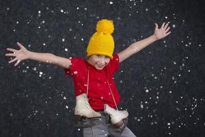 bonito pequeno Garoto dentro uma tricotado amarelo chapéu com vintage patins em uma cinzento fundo. foto