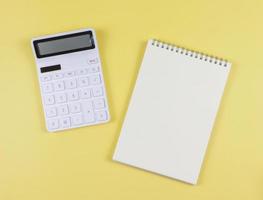plano deitar do branco calculadora com em branco página aberto caderno em amarelo fundo. o negócio e Educação conceito. foto
