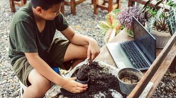 menino aprende a cultivar flores em vasos por meio de ensino online. cavando o solo em vasos para preparar as plantas para plantar o conceito de atividades de lazer foto